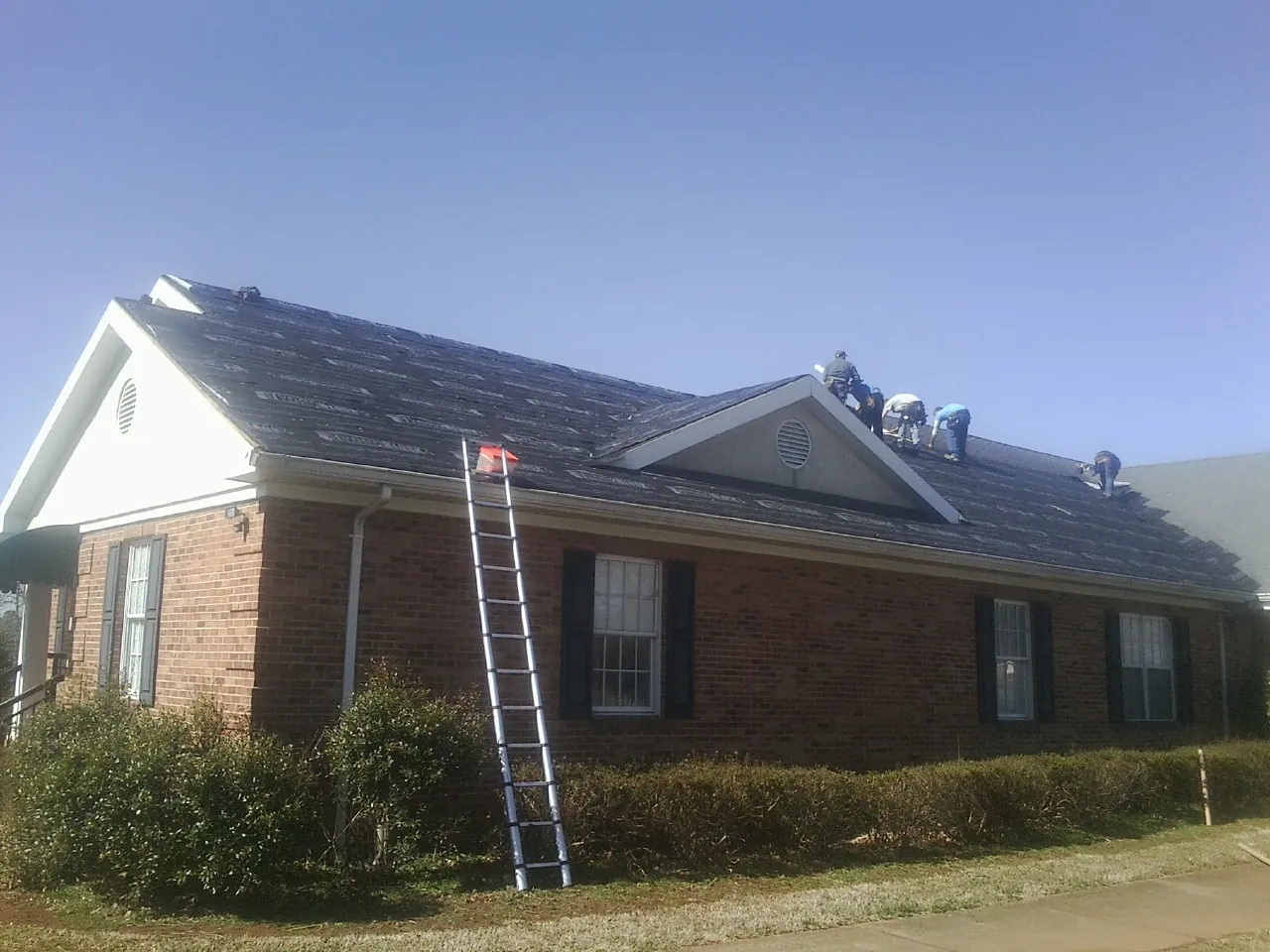 Crew tearing shingles off a brick ranch roof with a ladder set — Emergency Roof Repair work by our crew in Princeton Junction