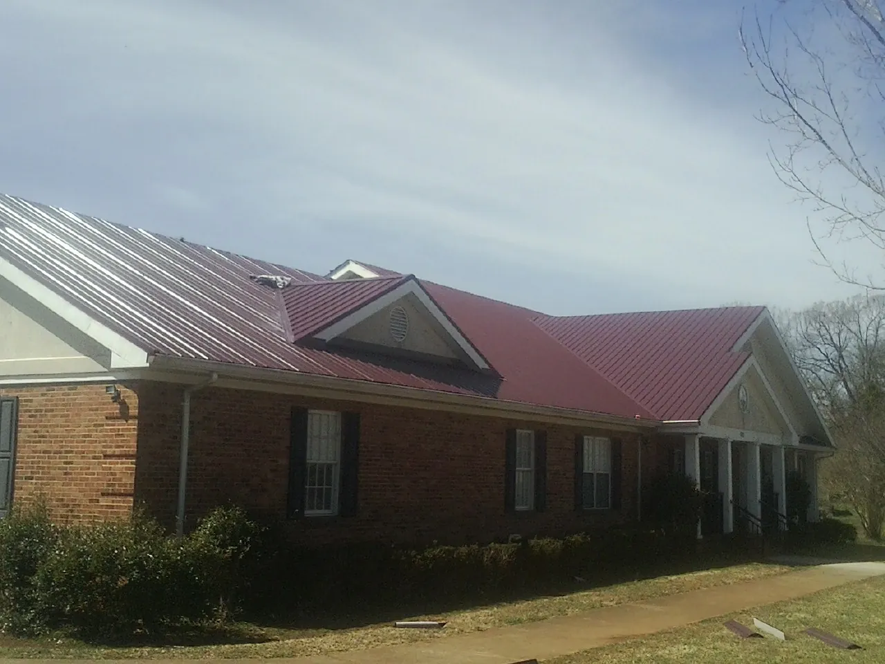 Red metal roof with gabled entries on a long brick building, from a Hail Damage Roof Repair job in Princeton Junction