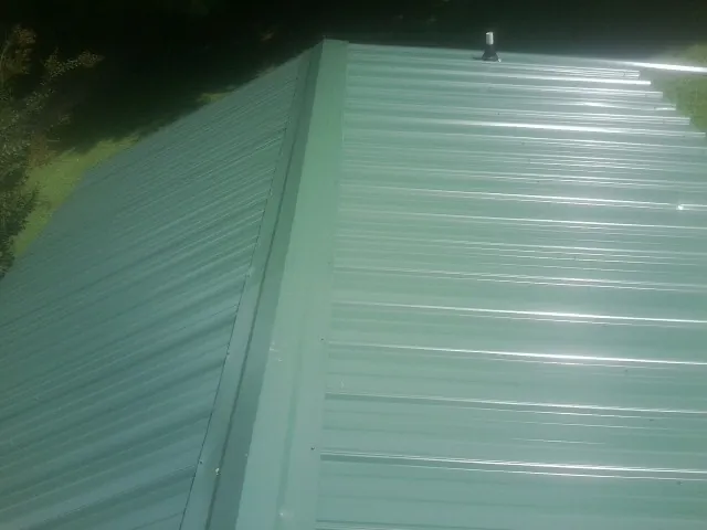 New green metal panels meeting at the ridge of a roof — Flat Roof Repair work by our crew in Princeton Junction