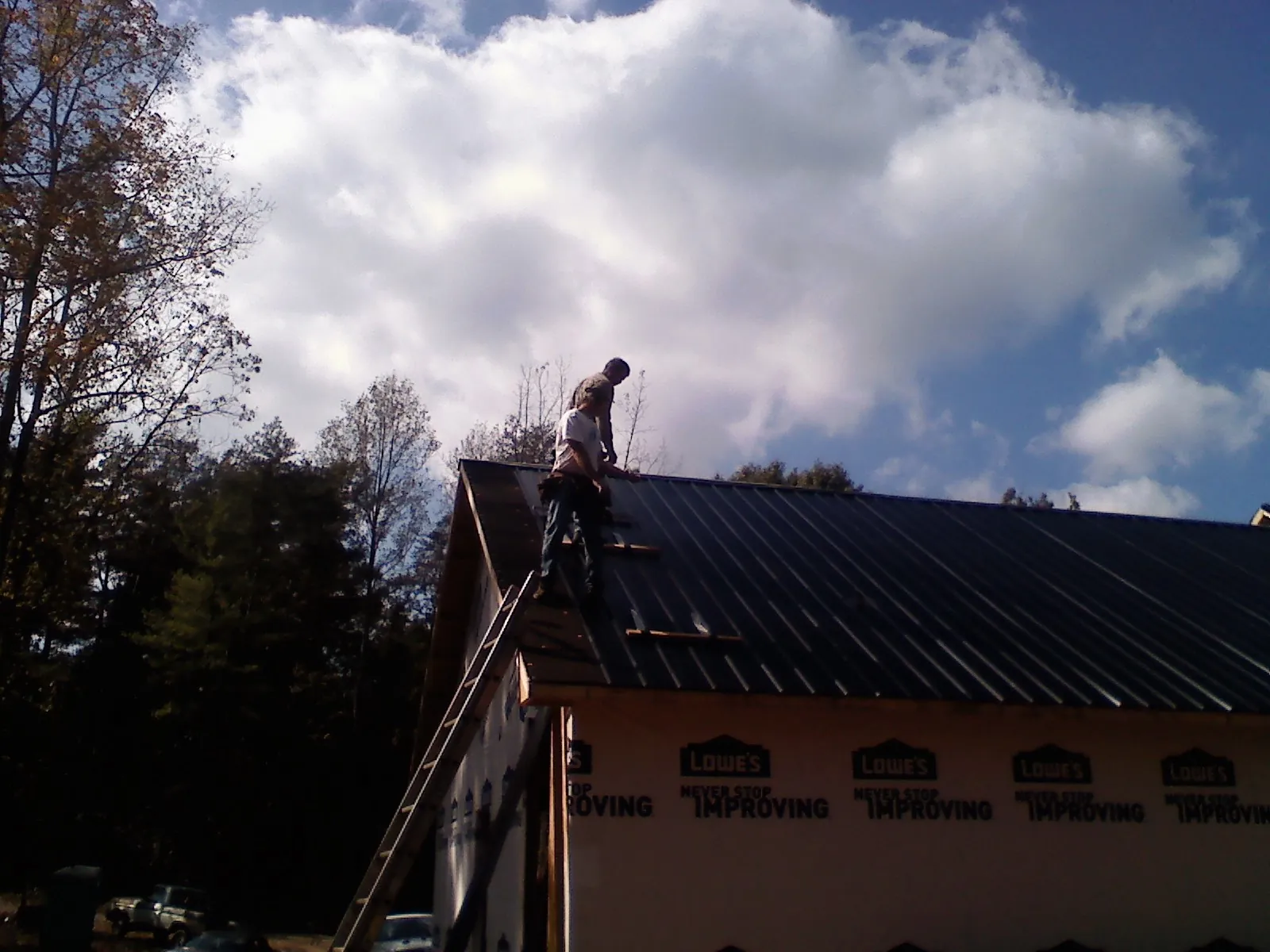 Roofer fastening dark metal panels high against a cloudy sky, from a Roof Inspection job in Princeton Junction
