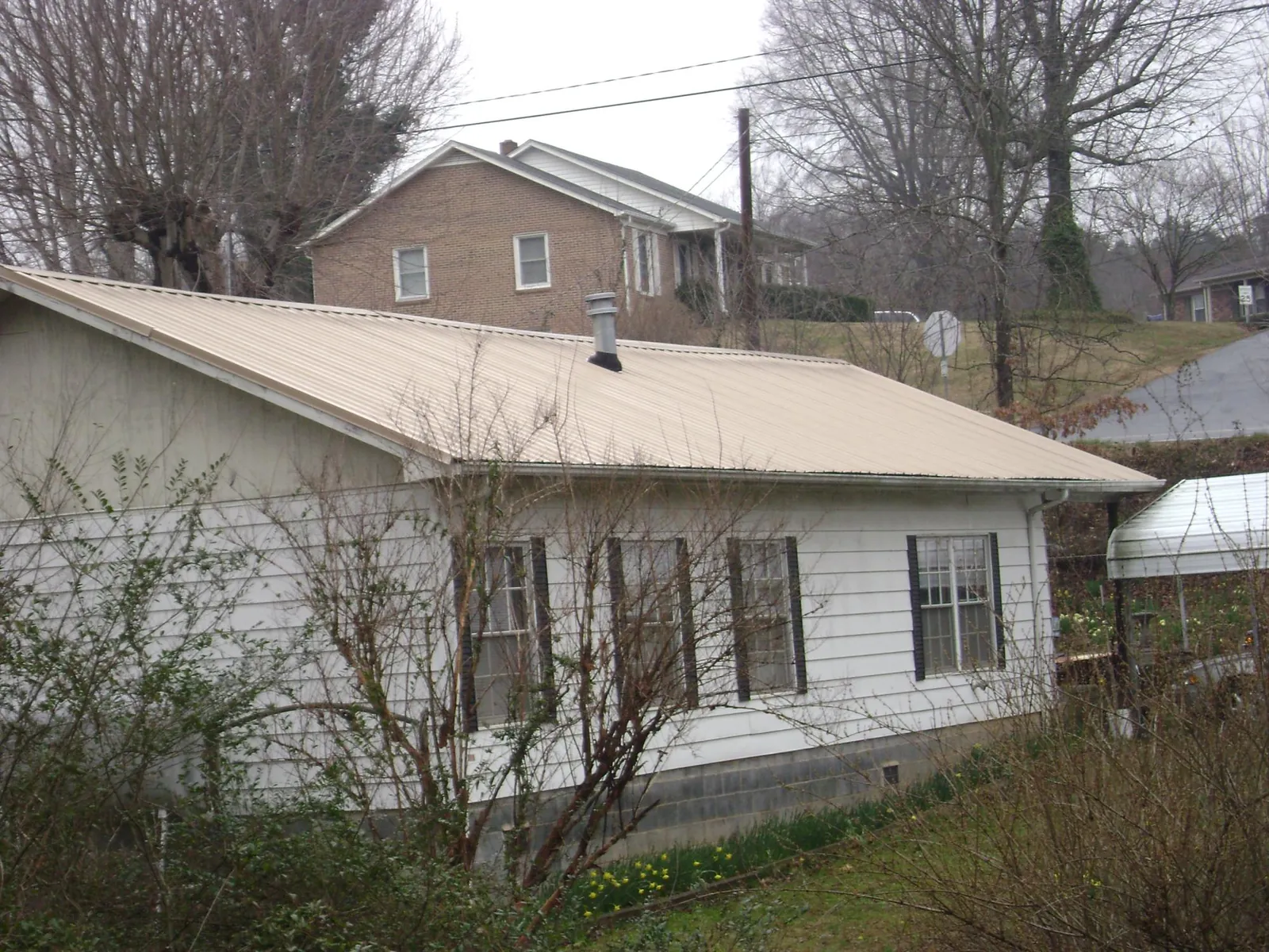 Tan metal roof on a white sided house set into a hillside — Commercial Roofing by Roofing Brothers in Princeton Junction